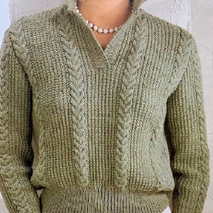 May include: A green knitted sweater with a cable knit pattern and a v-neck collar. The sweater has a ribbed hem and cuffs.