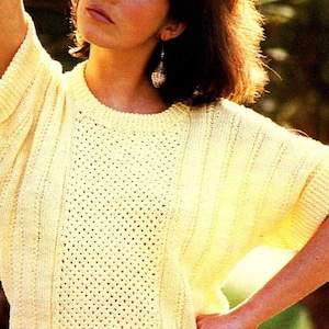 May include: A light yellow knit top with a round neckline and short sleeves. The top features a textured pattern with vertical ribbing and openwork detailing. The model is wearing a matching skirt.
