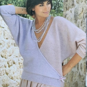 May include: A light purple and pink knitted sweater with a wrap style neckline and a bow detail at the waist.