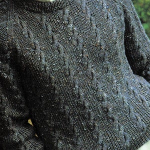 May include: A dark grey knitted jumper with a cable knit pattern. The jumper has a crew neck and long sleeves.
