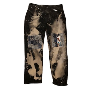 May include: Black denim jeans with bleach splatters and patchwork fabric on the knees.