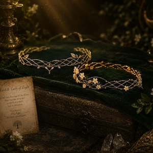 May include: Two gold-toned metal circlets featuring intricate lattice wirework. One circlet is plain with small leaf accents, while the other is adorned with small white flowers. A card with the text Lord & Lady of Light is visible nearby.