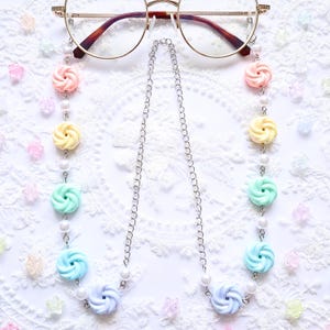 May include: A pastel-coloured glasses chain with a silver chain and colourful swirl beads in pink, yellow, green, and blue. The chain also features small white pearl beads. The glasses are gold-rimmed.