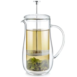 May include: A clear glass French press with a stainless steel plunger and lid. The press is filled with brewed tea and loose tea leaves. The handle is curved and the press is on a white background.