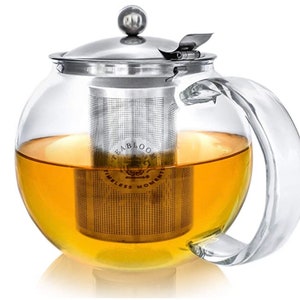 May include: A clear glass teapot with a stainless steel lid and infuser. The teapot is filled with a light amber tea and has the words "Teabloom Timeless Moments" printed on the infuser.