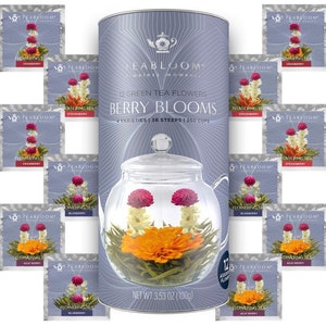 May include: A cylindrical container of Berry Blooms flowering tea with a glass teapot and individual tea sachets. The container is light blue with the text "TEABLOOM" and "BERRY BLOOMS." The sachets display various flowering tea varieties, including cranberry, strawberry, blueberry, and acai berry.