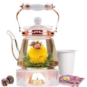 May include: A glass teapot with a rose and chrysanthemum blooming tea inside, a white ceramic teacup with a strainer, a white ceramic candle warmer with a pink floral design, and two blooming tea balls.