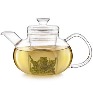 May include: A clear glass teapot with a curved handle and spout. The teapot contains a light yellow liquid and a bundle of green tea leaves. The lid and infuser are also made of clear glass.