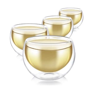 May include: Four clear double-walled glass cups filled with a light yellow liquid, likely tea or coffee. The cups are arranged in a row, with the closest cup in focus.