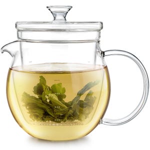 May include: A clear glass teapot with a curved handle and a lid. The teapot contains a light yellow liquid and green tea leaves. The teapot has a built-in infuser. The teapot is designed for brewing tea.