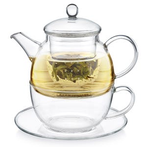 May include: A clear glass tea set with a teapot, infuser, cup, and saucer. The teapot contains brewed tea and loose tea leaves. The cup is placed on a saucer, and the set is designed for individual tea service.