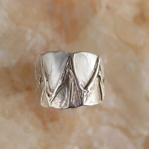 May include: A silver ring with a textured design featuring a series of overlapping triangles.