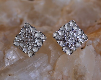May include: A pair of silver earrings with a textured, geometric design. The earrings are shaped like squares with a raised, textured surface.