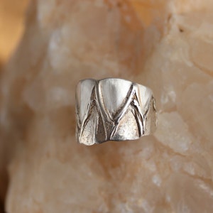 May include: A silver ring with a geometric design. The ring is made of a smooth, polished metal and has a unique, modern look.
