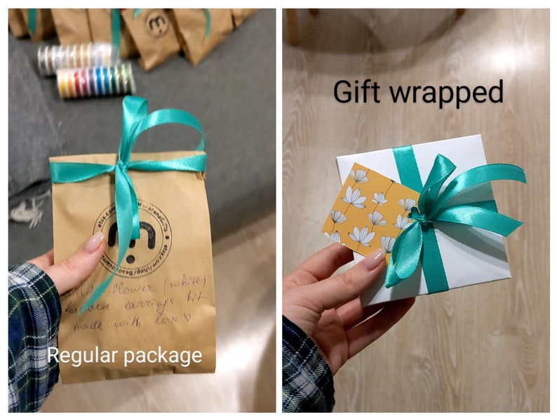 May include: Two images showing packaging options for a set of earrings. The first image shows a brown paper bag with a teal ribbon tied around it. The bag has a handwritten note that says "flower (white) beaded earrings kit made with love". The second image shows a white gift box with a teal ribbon tied around it. The box has a small yellow tag with white flowers on it.