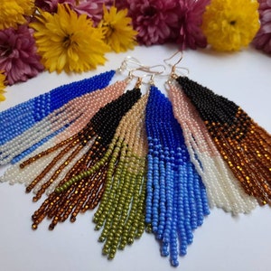 May include: A set of six pairs of long, beaded earrings. Each pair features a gradient of colors, including blue, pink, black, brown, green, and white.