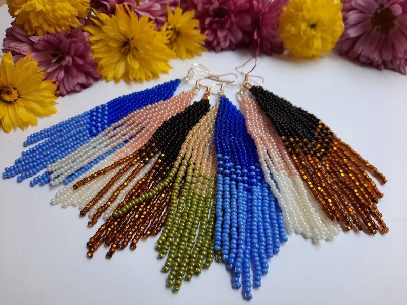 May include: A set of six pairs of long, beaded earrings. Each pair features a gradient of colors, including blue, pink, black, brown, green, and white.