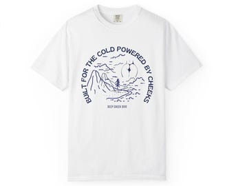 May include: White t-shirt with a navy blue graphic. The graphic features a mountain landscape with the text "BUILT FOR THE COLD POWERED BY CHEEKS" in a circular design. The text "DEEP CHEEK DIVE" is below the graphic.