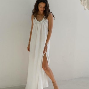 May include: A white maxi dress with a gathered neckline and a side slit. The dress is made of a lightweight, breathable fabric.