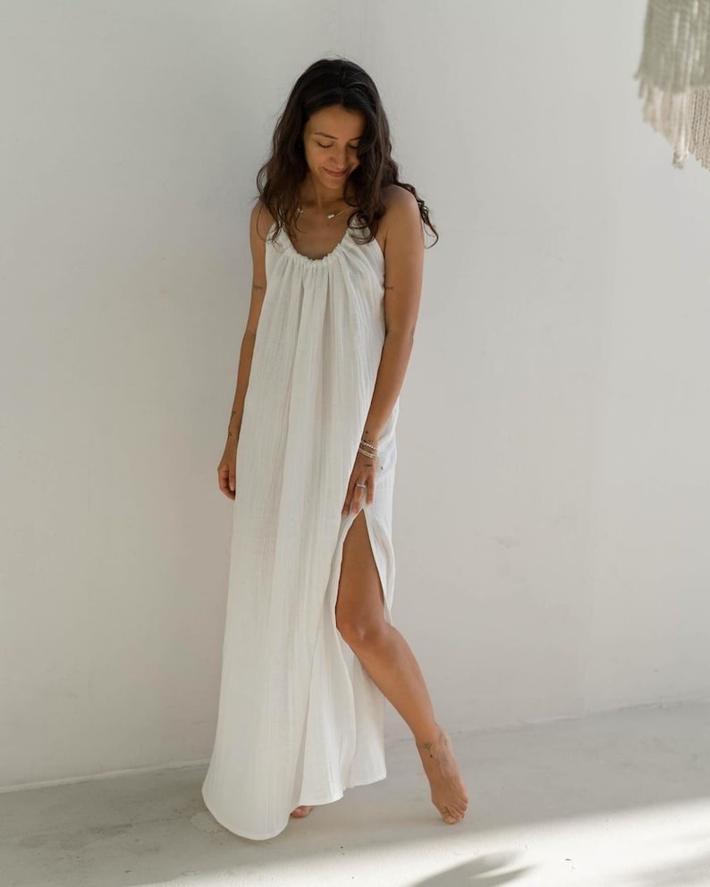 May include: A white maxi dress with a gathered neckline and a side slit. The dress is made of a lightweight, breathable fabric.