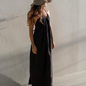 May include: A woman wearing a black maxi dress with a halter neckline and a wide-brimmed straw hat.