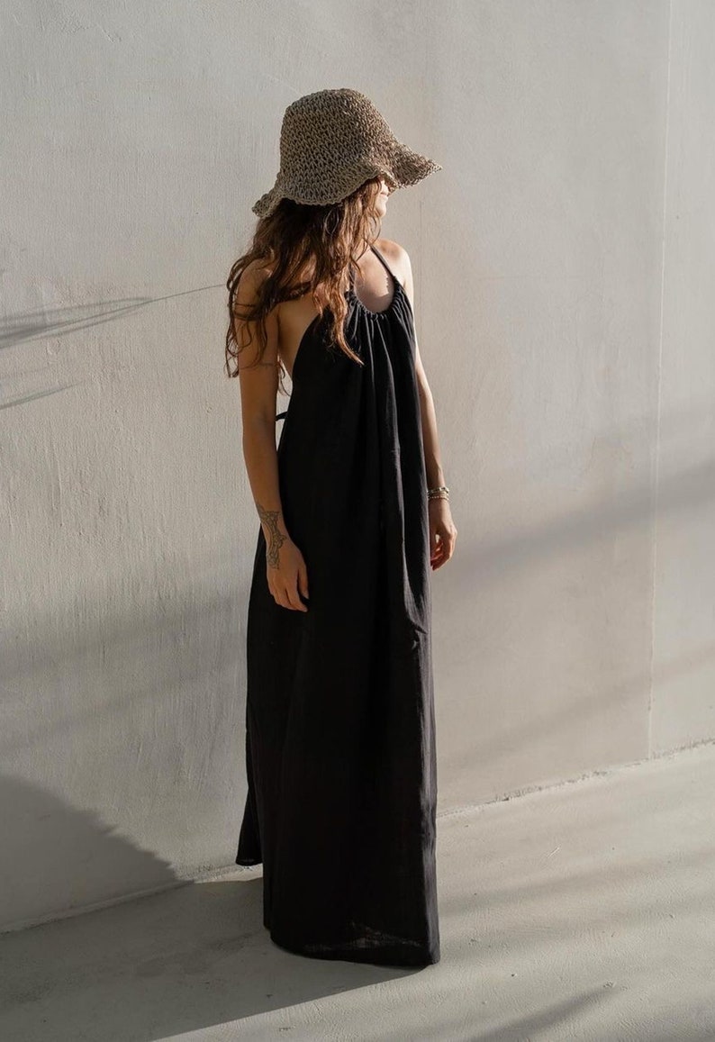 May include: A woman wearing a black maxi dress with a halter neckline and a wide-brimmed straw hat.