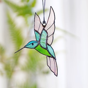 May include: A stained glass hummingbird ornament with pink, green, and blue accents. The hummingbird is in flight with its wings spread out.