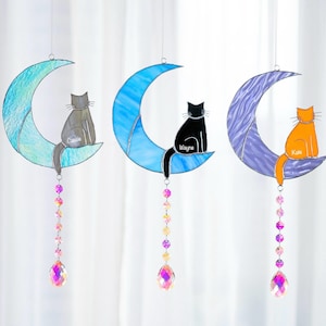 May include: Three stained glass moon and cat suncatchers with crystal beads hanging from the bottom. The moons are blue, purple, and green. The cats are gray, black, and orange. The cats' names are Cassie, Wayne, and Kitie.