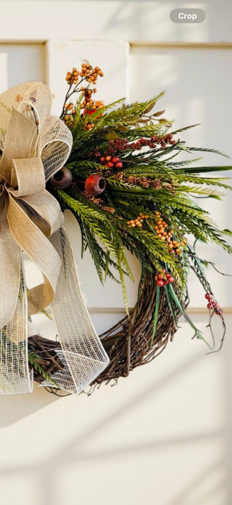 May include: A rustic wreath with a natural twig base, adorned with green foliage, red berries, and orange accents. A large burlap bow adds a touch of elegance. Perfect for seasonal home decor.