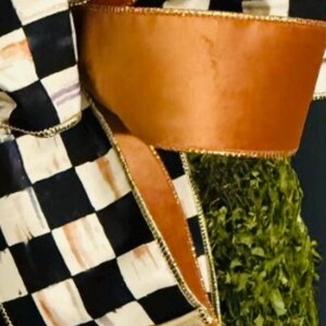 May include: A decorative bow featuring a black and white checkered pattern on one ribbon and a solid copper-colored ribbon. The ribbons have gold-toned wired edges and are arranged in multiple loops, partially obscuring a textured green base.