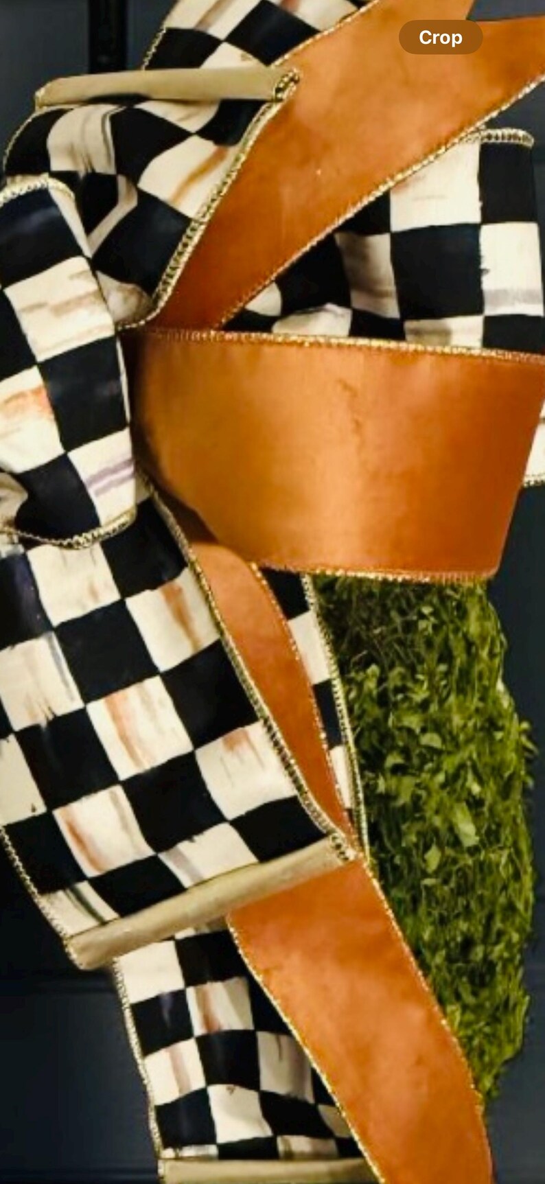 May include: A decorative bow featuring a black and white checkered pattern on one ribbon and a solid copper-colored ribbon. The ribbons have gold-toned wired edges and are arranged in multiple loops, partially obscuring a textured green base.