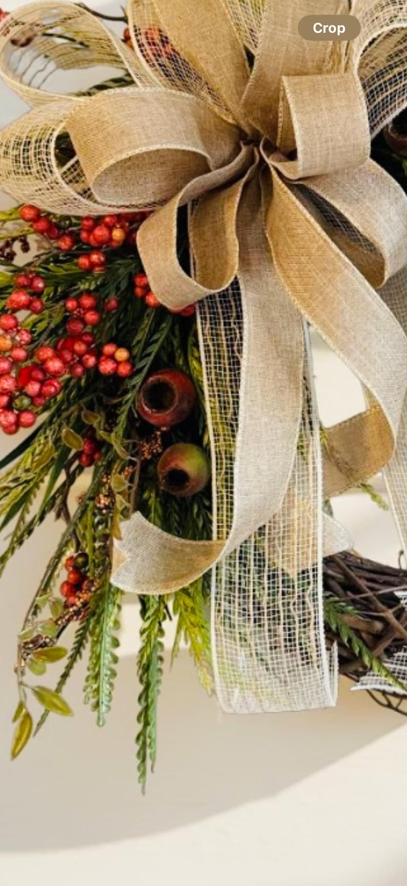May include: A rustic wreath featuring a large burlap bow with a woven texture. The wreath is adorned with red berries, green foliage, and decorative elements, creating a natural and inviting aesthetic.