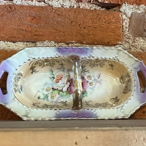 May include: A vintage porcelain serving dish with a divided centre and a handle. The dish is decorated with a floral pattern in shades of pink, purple, and green, and has a gold trim.