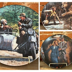 May include: Set of three decorative plates featuring scenes from an adventure film. One plate shows a man on a motorcycle with a sidecar, another depicts a man facing a lion, and the third shows a man and woman.