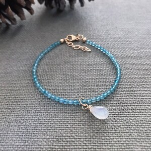 Pode incluir: Um delicado bracelete feito com pequenas contas de pedras preciosas azuis e um fecho dourado. Um pingente de pedra da lua em forma de lágrima pendura do bracelete.