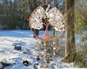 May include: A copper wire tree of life with white crystal beads and three crystal prisms hanging from the bottom. The tree is suspended from a copper wire loop.