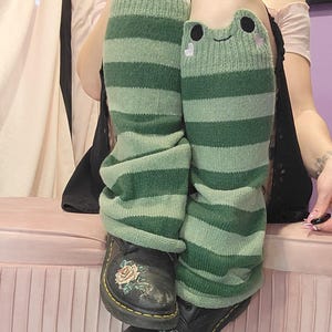 May include: Green and white striped knee-high socks with frog faces on the front. The socks are worn with black boots with floral embroidery.