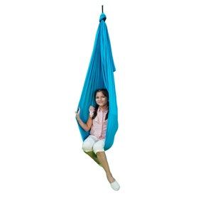 Peut inclure: Une jeune personne est assise dans une balançoire en tissu bleu suspendue au plafond. La balançoire est faite d'un tissu doux et extensible et est conçue pour une utilisation en intérieur.