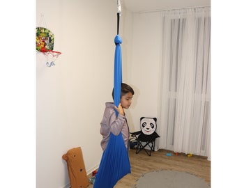 Pode incluir: Uma criança está sentada em um balanço de tecido azul pendurado no teto. O balanço é feito de tecido macio e elástico e é projetado para uso interno.