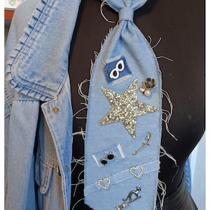 Può includere: Cravatta in denim blu chiaro impreziosita da una grande stella scintillante e vari elementi decorativi. La cravatta è abbinata a una giacca di jeans coordinata, creando un ensemble unico ed elegante.