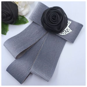 Cravatta da donna, elegante, stilosa, accessorio di abbigliamento bellissimo. Il colore è grigio, con una spilla a forma di rosa nera.