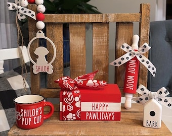 May include: A wooden bench with a red and white gift box that says "Happy Pawlidays". There is a red mug with the words "Shiloh's Pup Cup" on it, a rolling pin with the words "Woof Woof" on it, and a white wooden house with the word "Bark" on it.