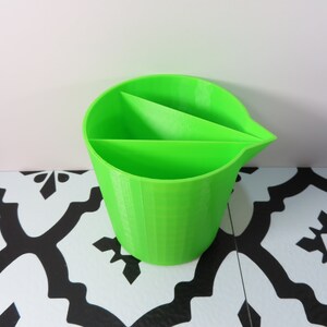 May include: A bright green plastic container with three divided sections. The container has a smooth, rounded exterior and a textured, striped interior.