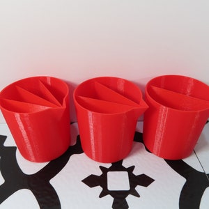 May include: Three red plastic cups with three sections each. The cups are on a black and white tiled surface.