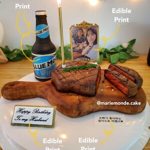 May include: A birthday cake decorated with a chocolate steak, a bottle of beer, and a photo of a couple. The cake is on a white plate and has a sign that says "Happy Birthday to my Husband".