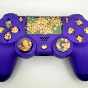 May include: A purple PlayStation 4 controller with custom face buttons and thumbsticks. The face buttons and thumbsticks have a glittery, iridescent finish with orange and yellow flecks.