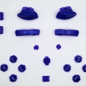 May include: A set of purple replacement buttons for a video game controller. The set includes face buttons, shoulder buttons, and directional pad buttons.