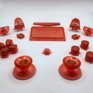May include: A set of red replacement buttons for a video game controller. The set includes a d-pad, face buttons, shoulder buttons, analog stick caps, and a control panel.