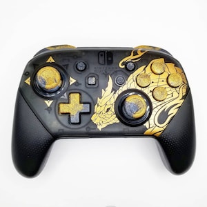 May include: Black Nintendo Switch Pro Controller with gold accents. The controller features a gold dragon design on the right side and gold glitter on the buttons. The Nintendo Switch logo is visible.