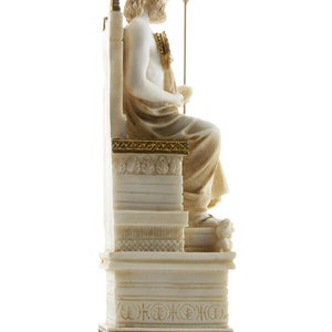 Op de afbeelding: Wit marmeren beeld van Zeus, de Griekse god van de hemel en de donder, zittend op een troon met een gouden kroon en scepter. Het beeld staat op een witte marmeren voet met gouden accenten.